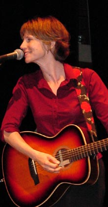 Tracy Grammer, smiling, singing and playing guitar